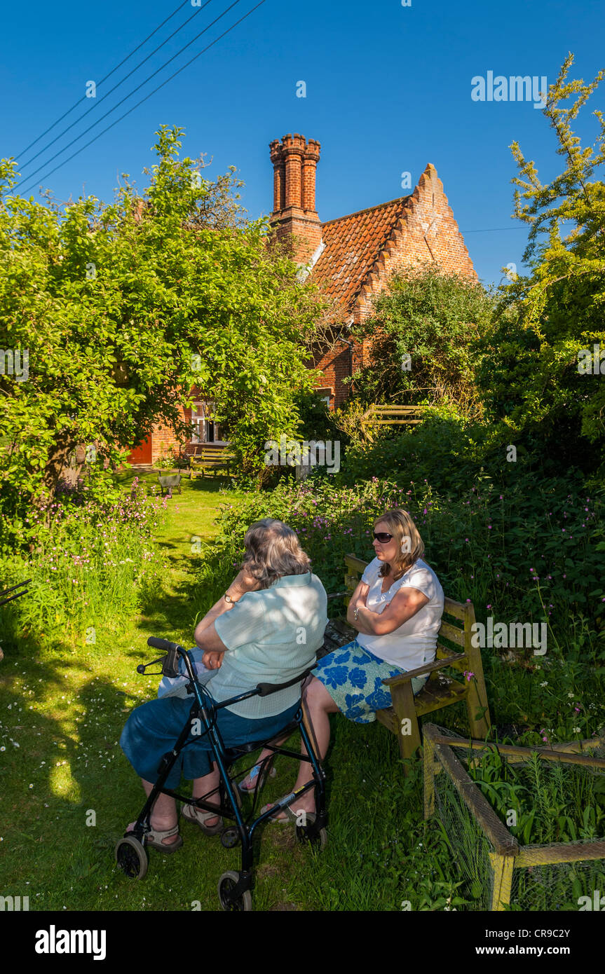 Una donna nel suo 30's parla a sua madre di diritto nel suo 70's in un Regno Unito Garden cottage Foto Stock