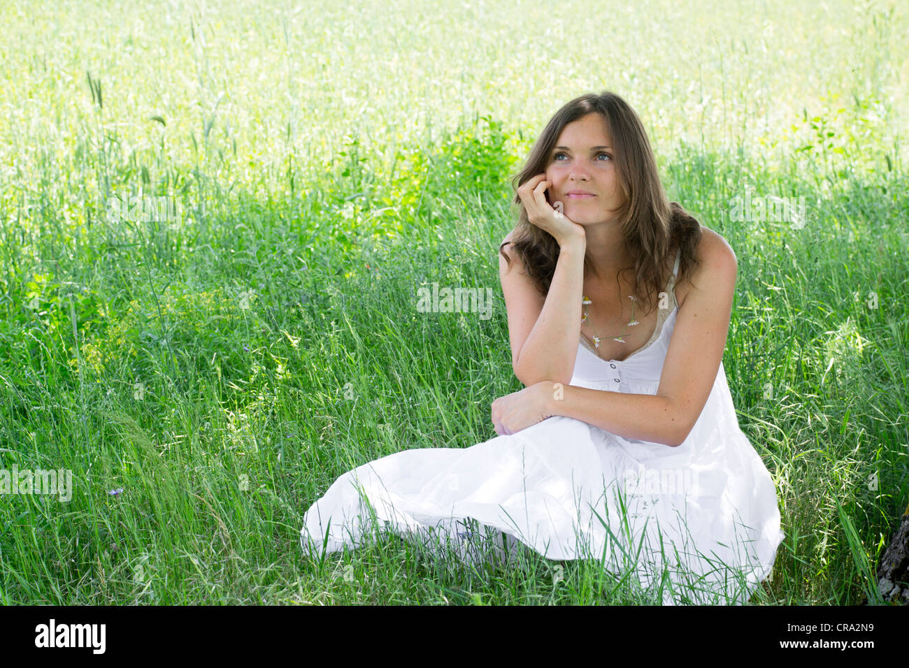 Una donna seduta in un prato sorride a se stessa mentre fantasticando Foto Stock