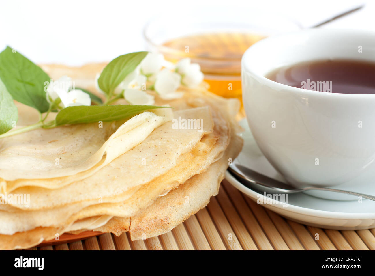 Frittelle con miele e tè nero in una tazza bianca, fiori di gelsomino sulla sommità di frittelle Foto Stock