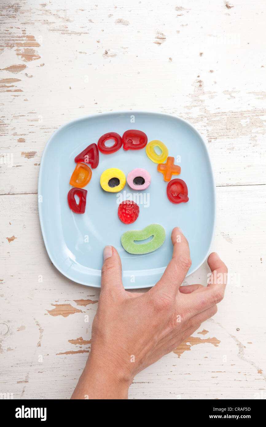 La mano di raggiungere per caramelle, faccia fatta di orsi gommoso, cibo per bambini Foto Stock