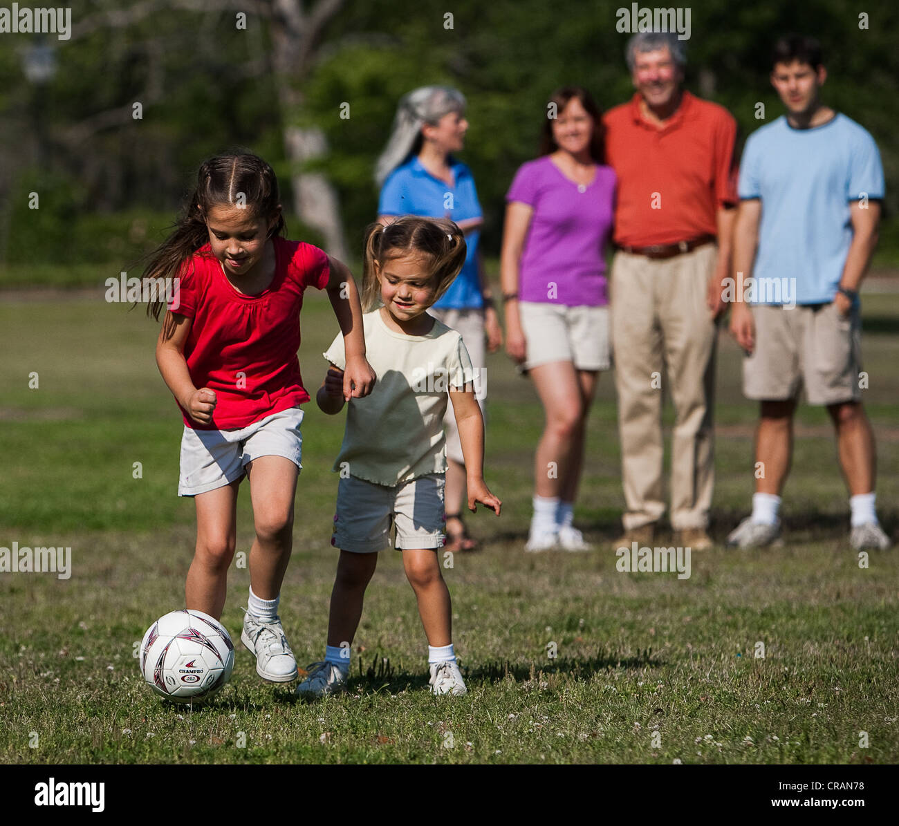Sorelle giocare a calcio mentre la famiglia orologi al parco locale. Foto Stock