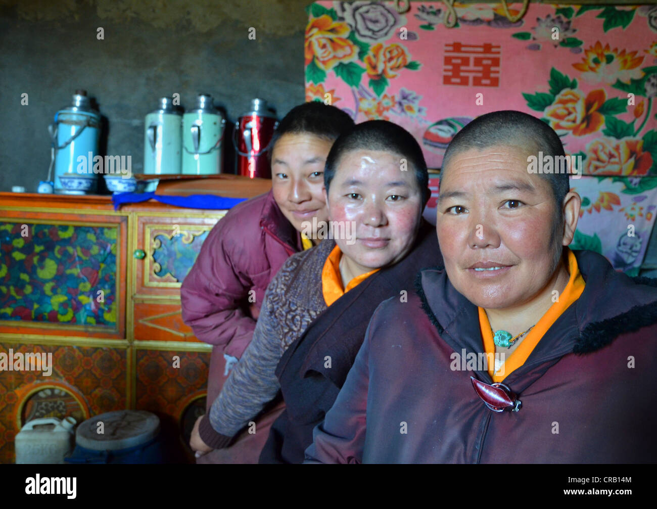 Tibetano tre monache seduta nella cucina del convento di fronte thermos per il burro tè, nelle montagne del Foto Stock