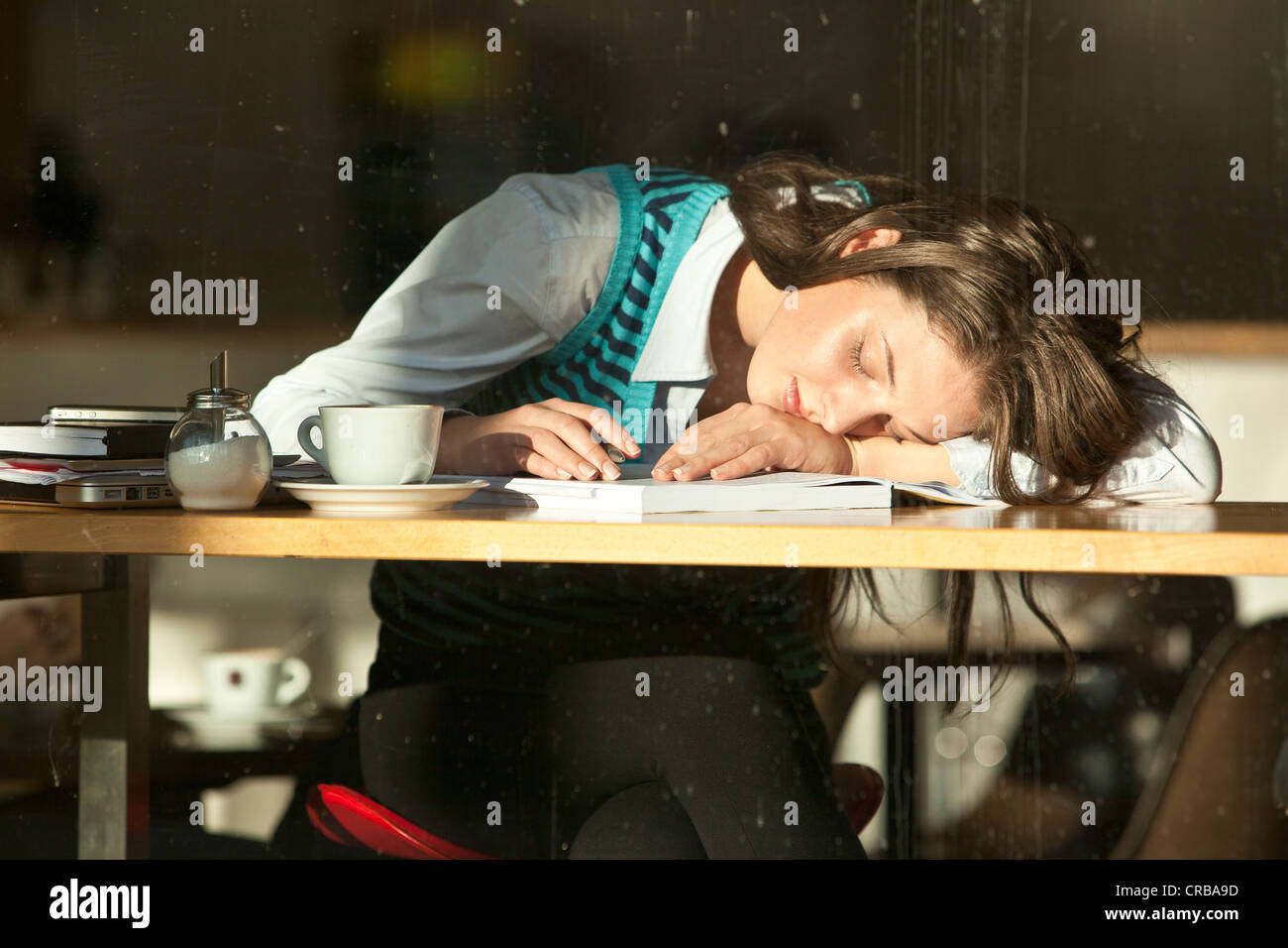 Studente seduto in un bar, lei è caduto addormentato oltre le sue note, visibile attraverso una finestra Foto Stock