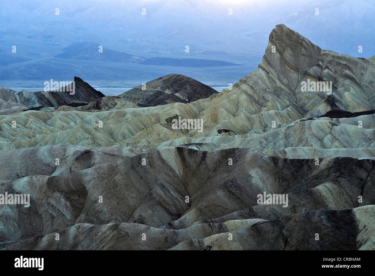 Vista da Zabriskie Point a Manly Beacon con rocce erose scolorito da minerali, Panamint Range al retro, crepuscolo Foto Stock