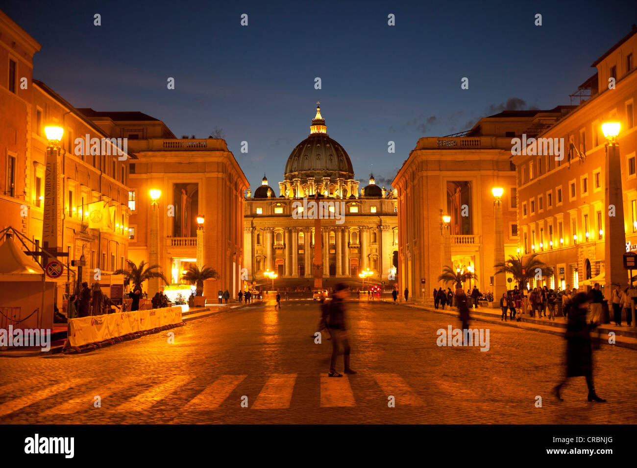 Pedoni che attraversano la Via della Conciliazione, la strada della riconciliazione, illuminato dalla Basilica di San Pietro sul retro, Roma, Italia Foto Stock