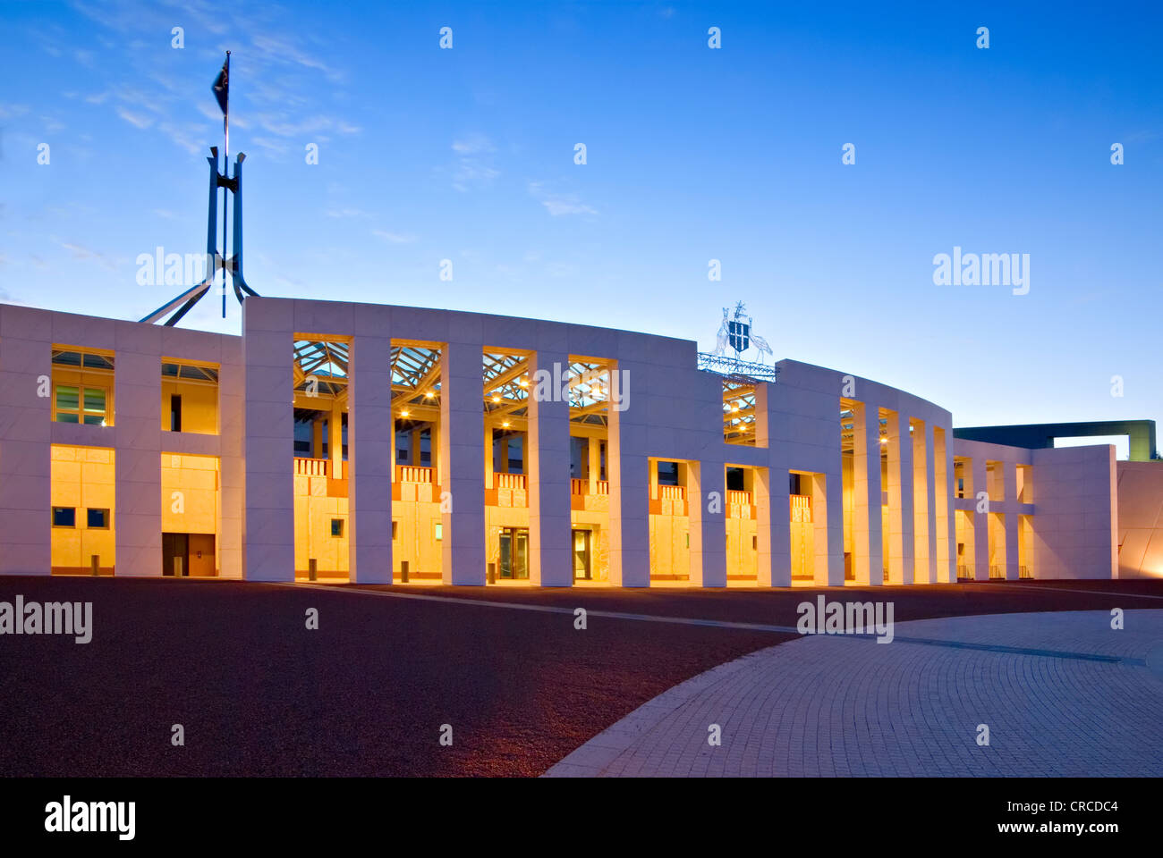 Parlamento australiano casa illuminata al crepuscolo. Una leggera sfocatura sulla bandiera a causa di una lunga esposizione. Foto Stock
