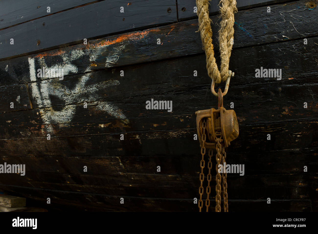 Una puleggia della catena si blocca oltre il lato di una vecchia barca di legno in fase di restauro Foto Stock