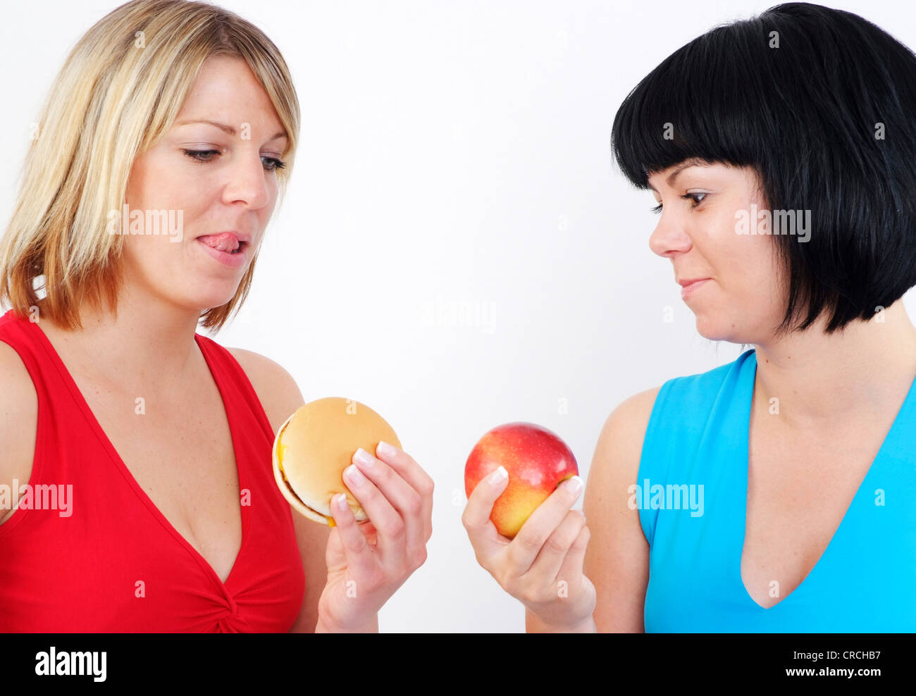 Due donne con burger e Apple. Il dai capelli scuri con Apple, guardando con interesse a hamburger della donna bionda e viceversa Foto Stock