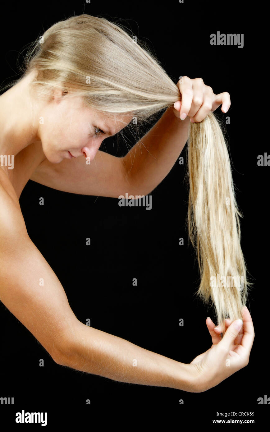 Giovane biondo e longhaired donna controlla i suoi capelli suggerimenti Foto Stock