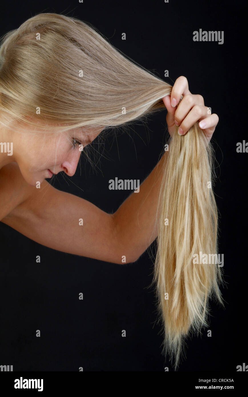 Giovane biondo e longhaired donna controlla i suoi capelli suggerimenti Foto Stock