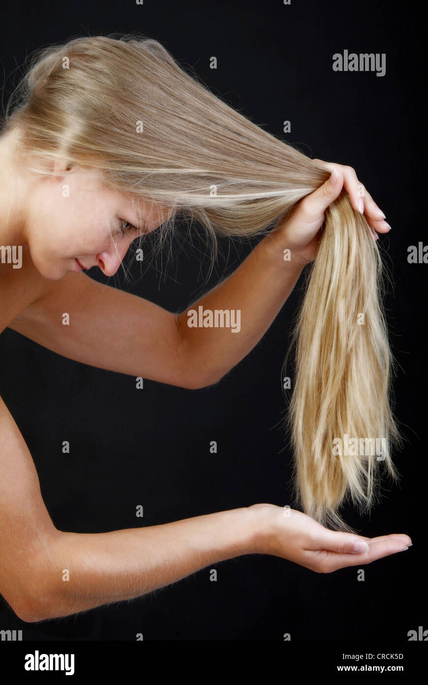 Giovane biondo e longhaired donna controlla i suoi capelli suggerimenti Foto Stock