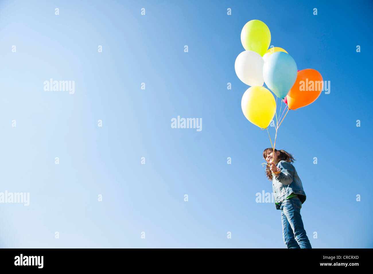 Ragazza in piedi con palloni sotto il cielo blu Foto Stock