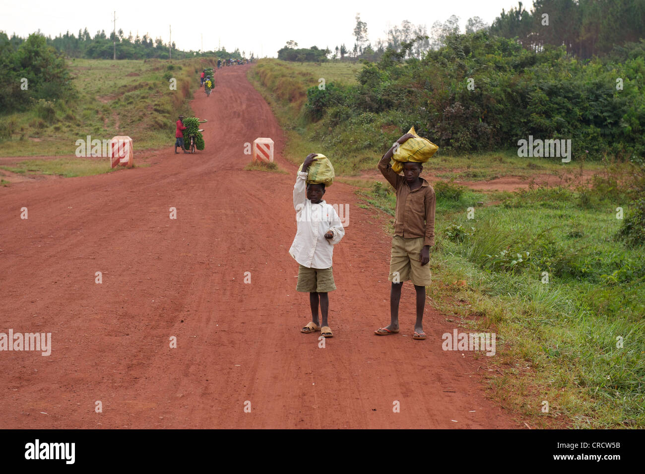 I bambini che trasportano carichi sulle loro teste su una strada nei pressi di Bukoba, Tanzania Africa Foto Stock