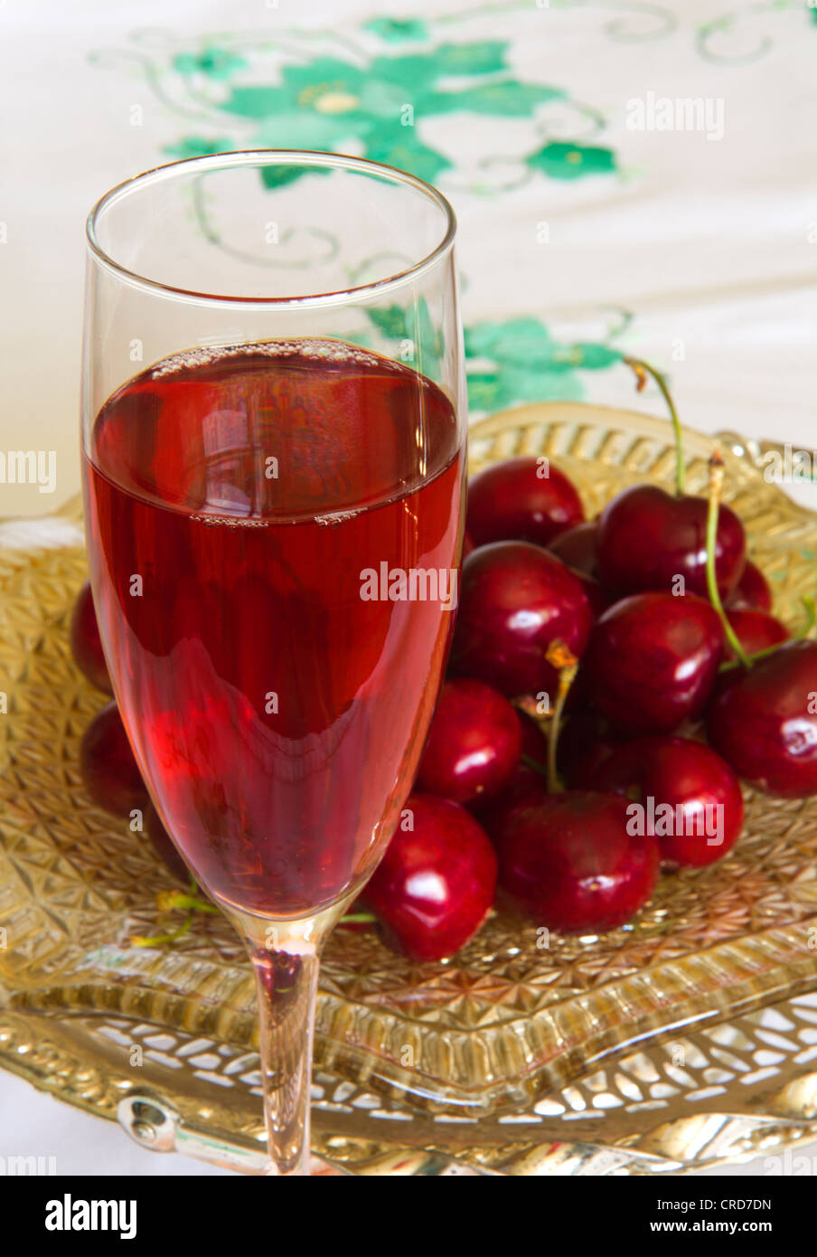 Succhi di frutta in vetro con ciliegie su un piatto di vetro, su una verde applique tovaglia ricamata. Foto Stock