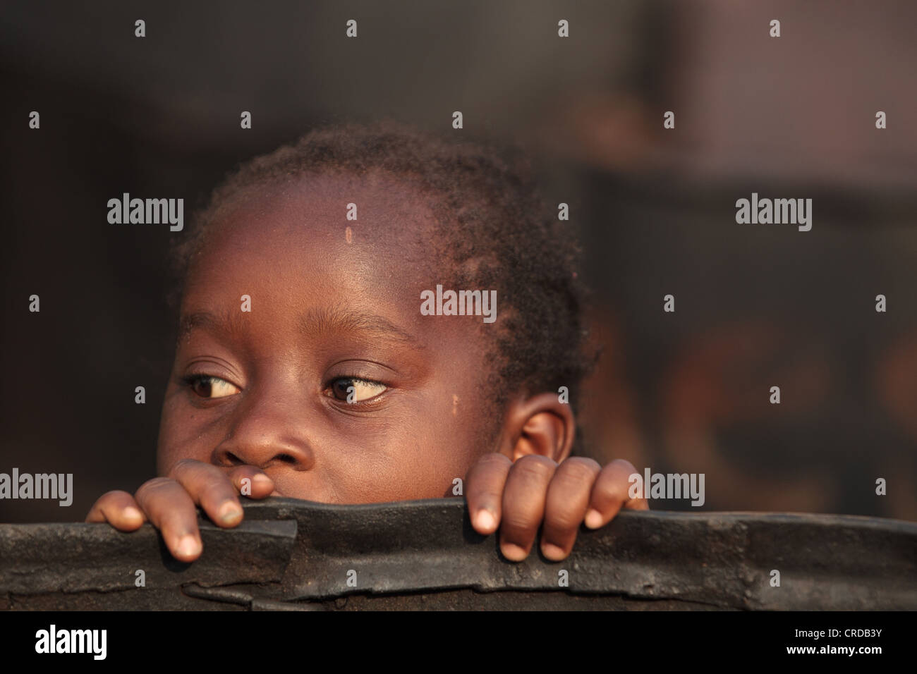 Una ragazza picchi da dietro una grande botte usata per fumare pesce nel West Point baraccopoli di Monrovia, Montserrado county, Liberia Foto Stock