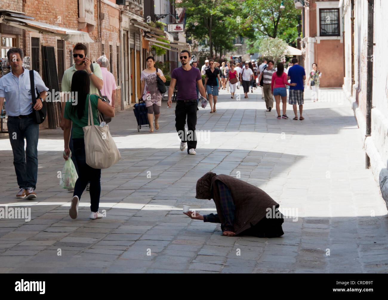 Una donna a mendicare per le strade di Venezia tra il passaggio di turisti Foto Stock