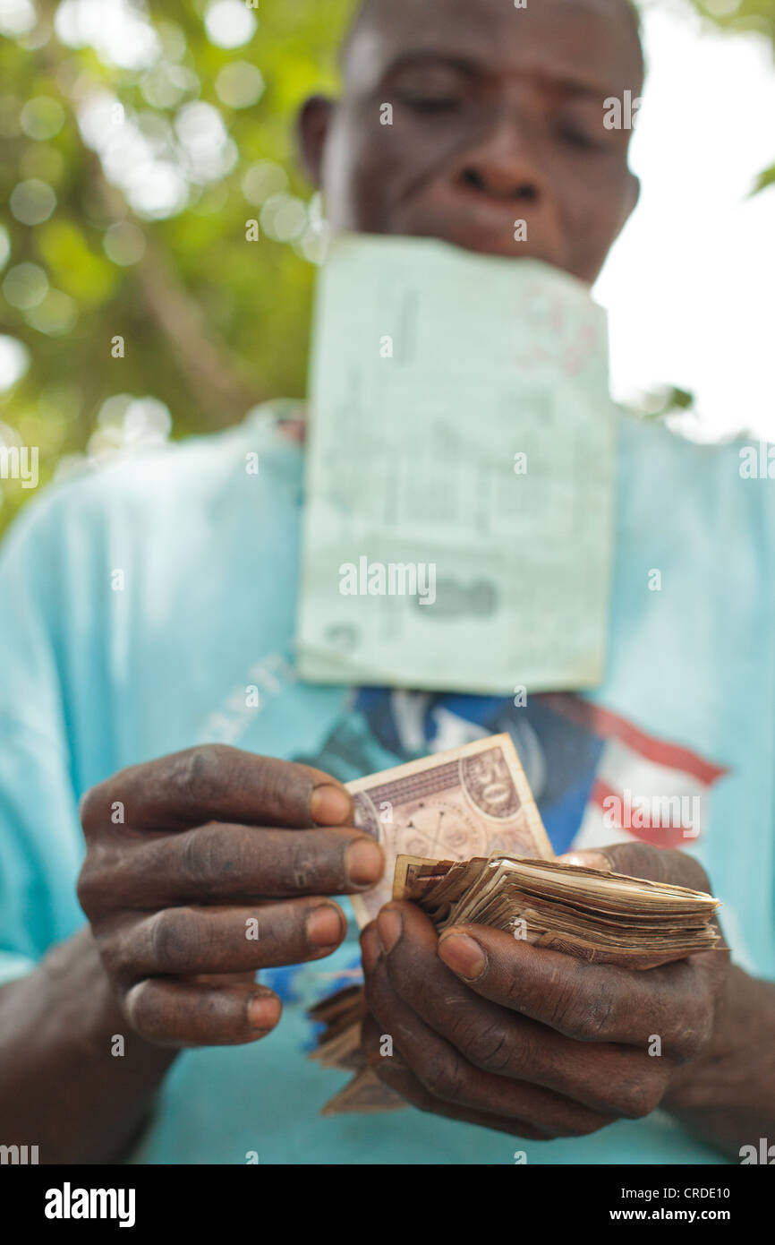 Un uomo conta i soldi che ha appena ricevuto da una cassa sociale programma di trasferimento nel villaggio di Julijuah, Liberia Foto Stock