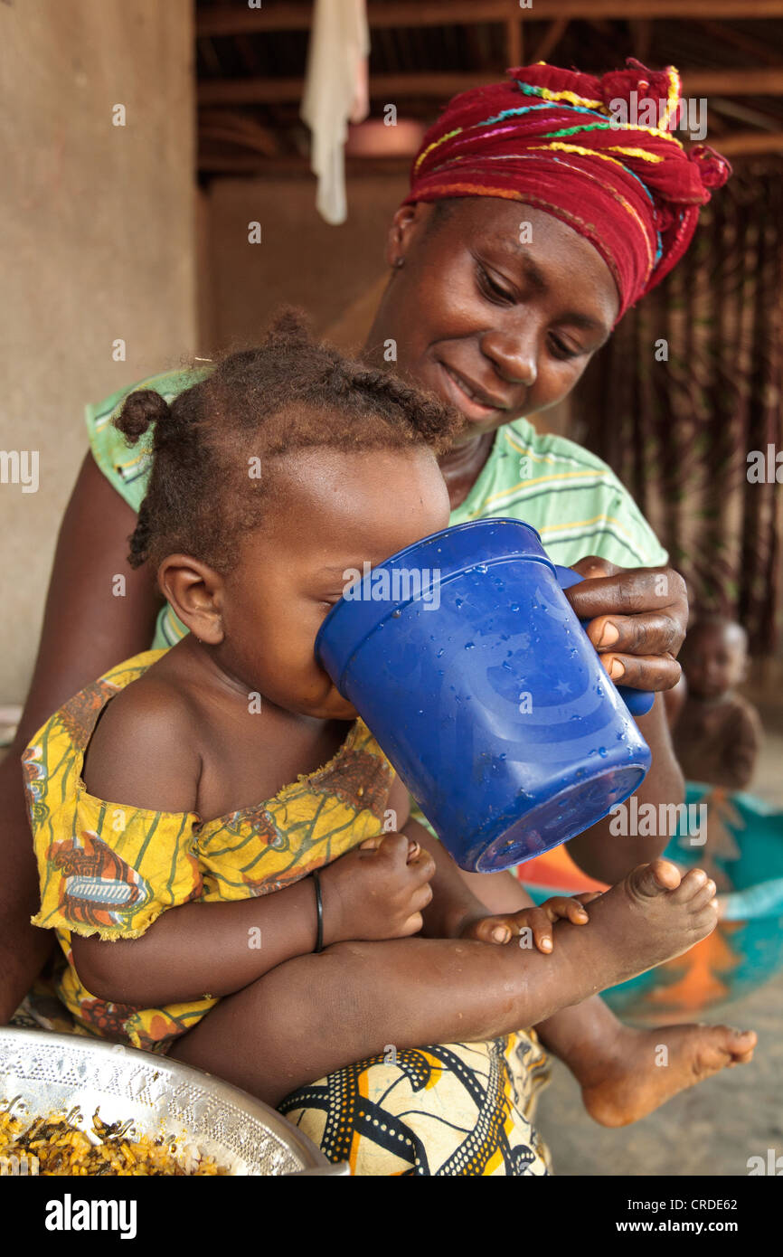 Jenneh Johnson, 31, fornisce acqua da bere a sua figlia Jusu, 2, a casa nel villaggio di Julijuah, Contea Bomi, Liberia. Foto Stock