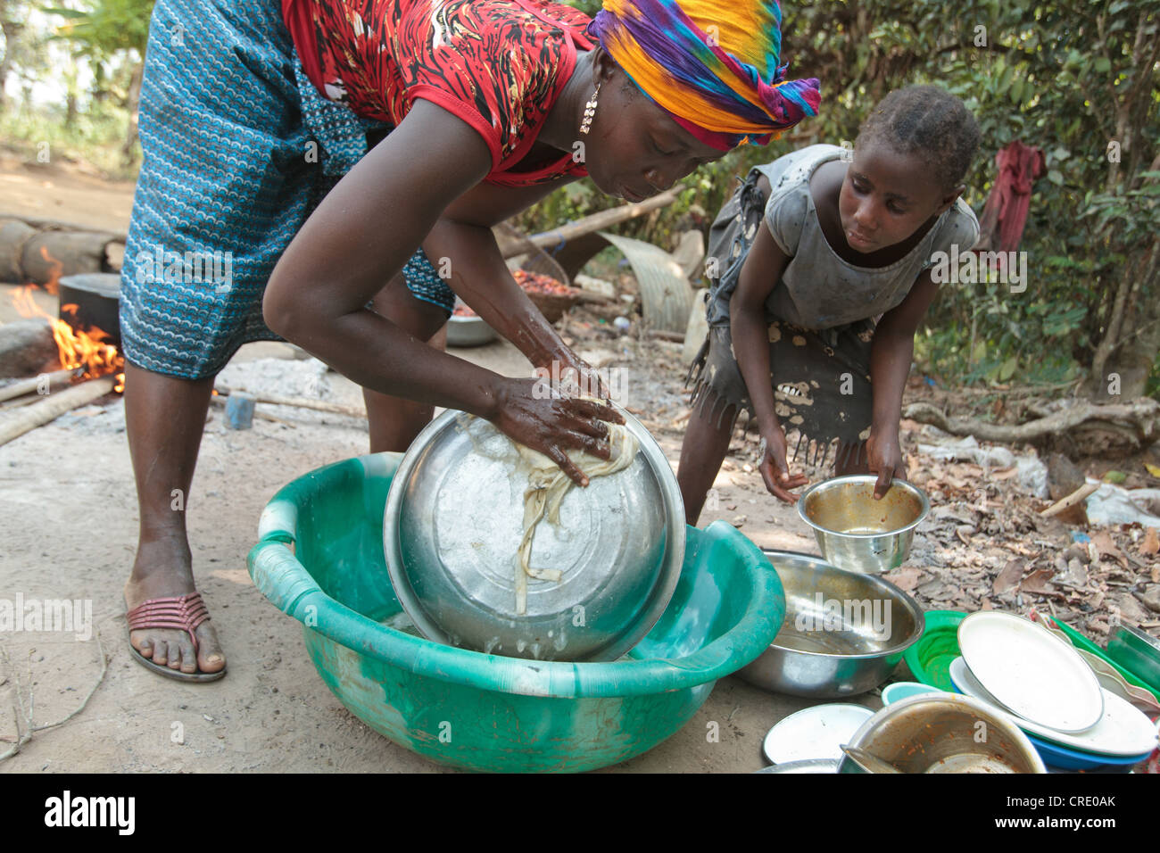 Tarah, 7, aiuta a sua madre Edith Saysay, 35, piatti puliti al di fuori della loro casa nel villaggio di Jenneh, Contea Bomi, Liberia Foto Stock