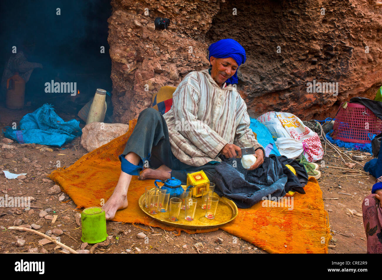 Berber uomo che indossa un turbante blu utilizzando una lama metallica per radere i pezzi di zucchero per il suo tè, nomade abitante della grotta Foto Stock
