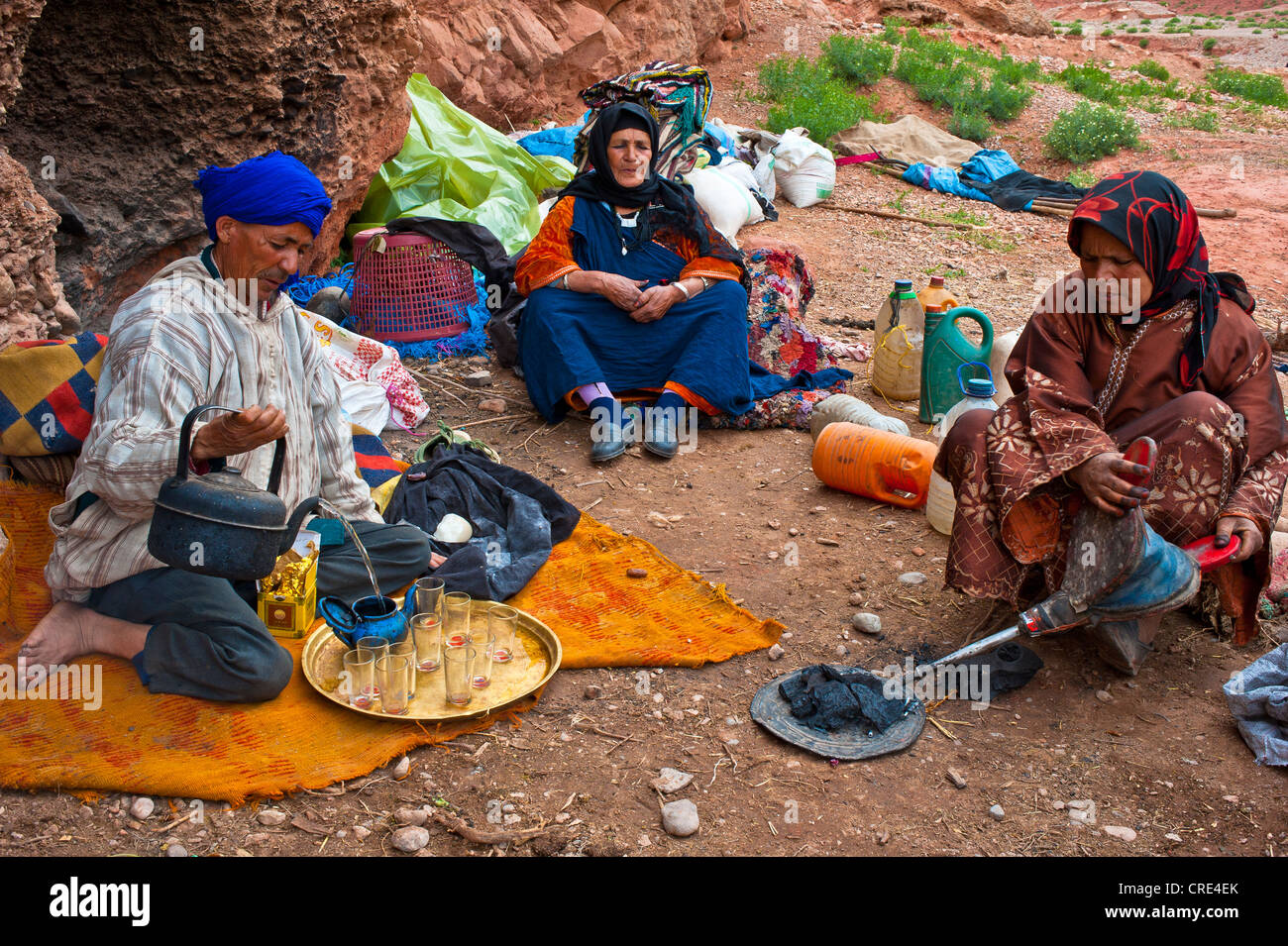 Grotta di nomadi-abitatori, Berber, un uomo che indossa un turbante blu è versando una tazza di tè, una donna è usando soffietto per mantenere il Foto Stock