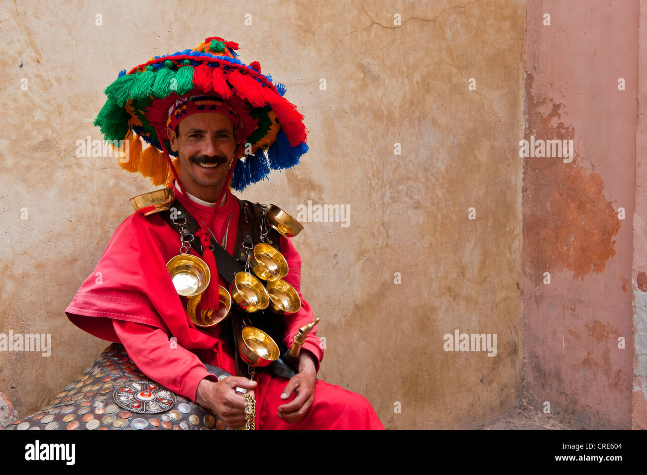 Vettore acqua, indossando abiti tradizionali e ciotole di acqua in ottone, seduto contro un muro, Marrakech, Marocco, Africa Foto Stock