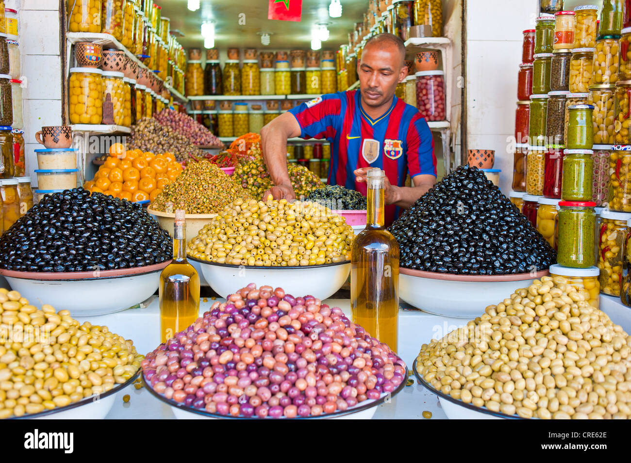 Merchant che offrono vari tipi di olive, olio d'oliva nei piatti e bicchieri in vendita presso il suo stand, souk, Bazaar, Marrakech, Marocco Foto Stock