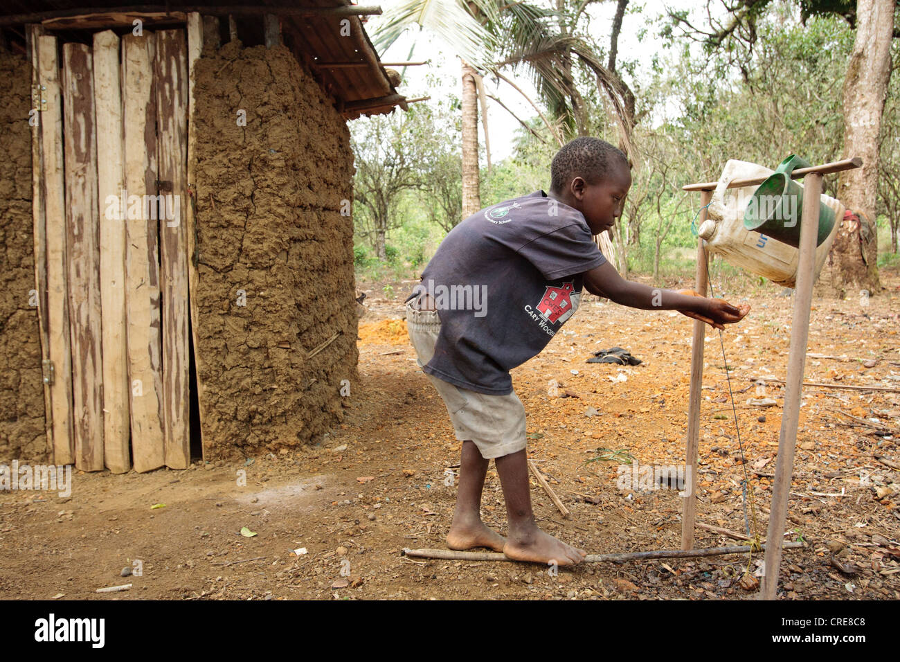 Un ragazzo si lava le mani in un pedale azionato a mano la stazione di lavaggio al di fuori di una latrina di casa nel villaggio di Kawejah Foto Stock