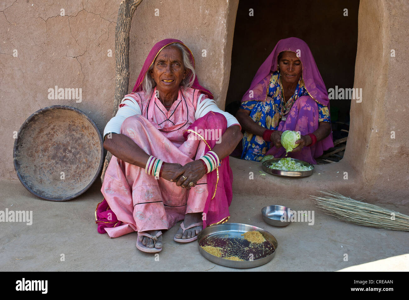 Un'anziana donna indiana indossando un sari seduta sul pavimento di fronte a un ingresso di casa, una giovane donna è seduto alla porta Foto Stock
