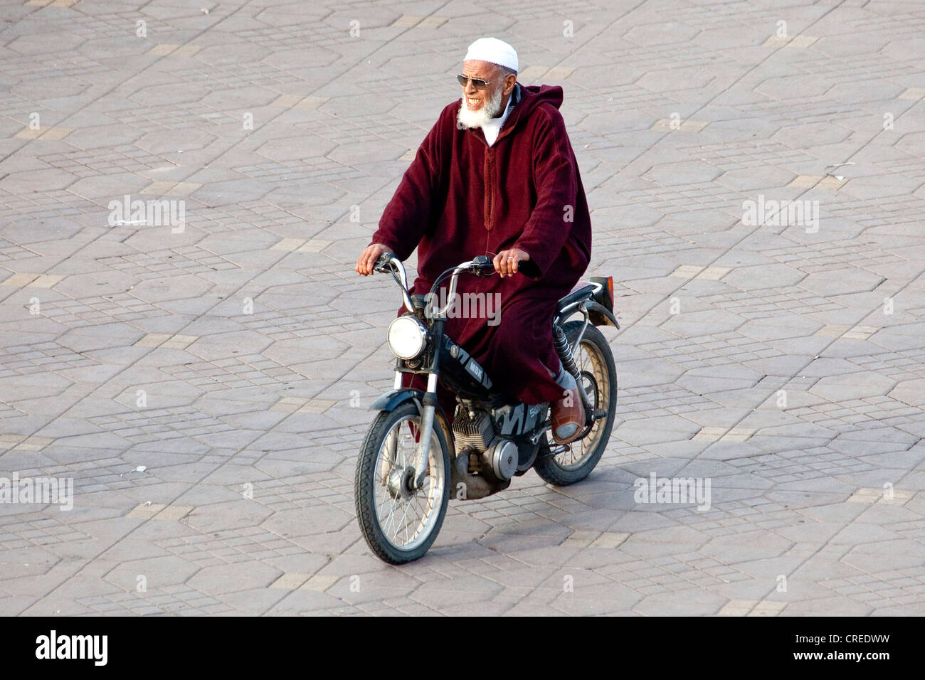 Uomo a cavallo di un ciclomotore indossando un djellaba tradizionale in Djemaa El Fna, medina o città vecchia, Patrimonio Mondiale dell UNESCO Foto Stock