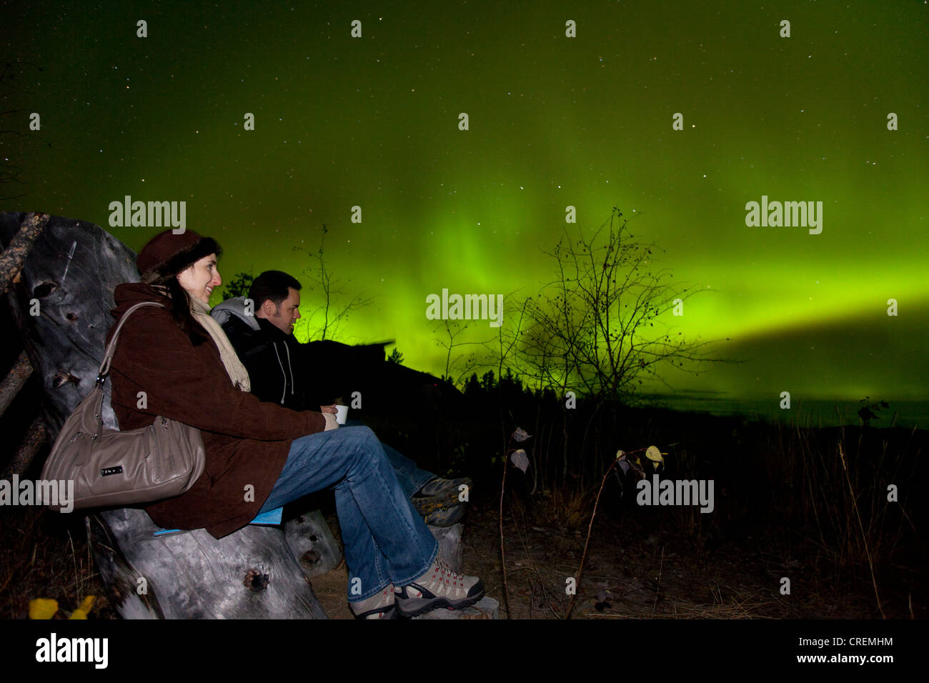 Giovane, donna e uomo seduto in una sedia in legno, guardando la roteazione Northern Lights, Aurorae polare, Aurora Boreale, verde Foto Stock