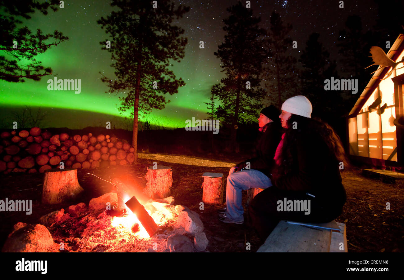 Coppia giovane, donna e uomo, seduta in corrispondenza di un fuoco di campo, falò, guardando la Northern Lights, polari o aurora Aurora Boreale, verde Foto Stock