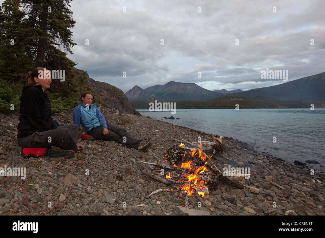 Due giovani donne sedute in corrispondenza di un fuoco di campo, riva del lago Atlin, British Columbia, Canada, America Foto Stock