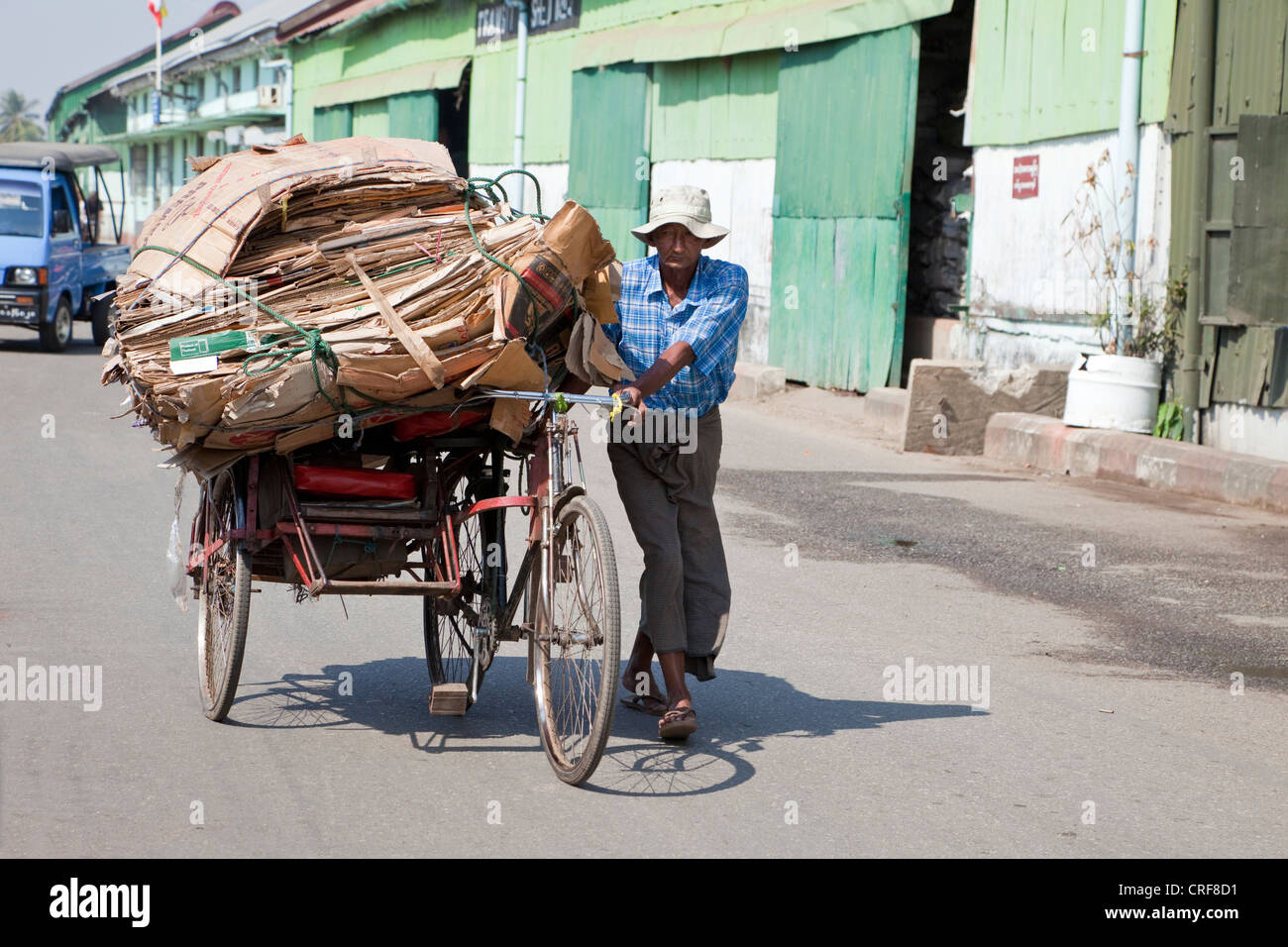 Myanmar Birmania, Yangon. Il riciclaggio. In rickshaw Driver passeggiate un carico di cartoncino ad una stazione di riciclaggio. Foto Stock