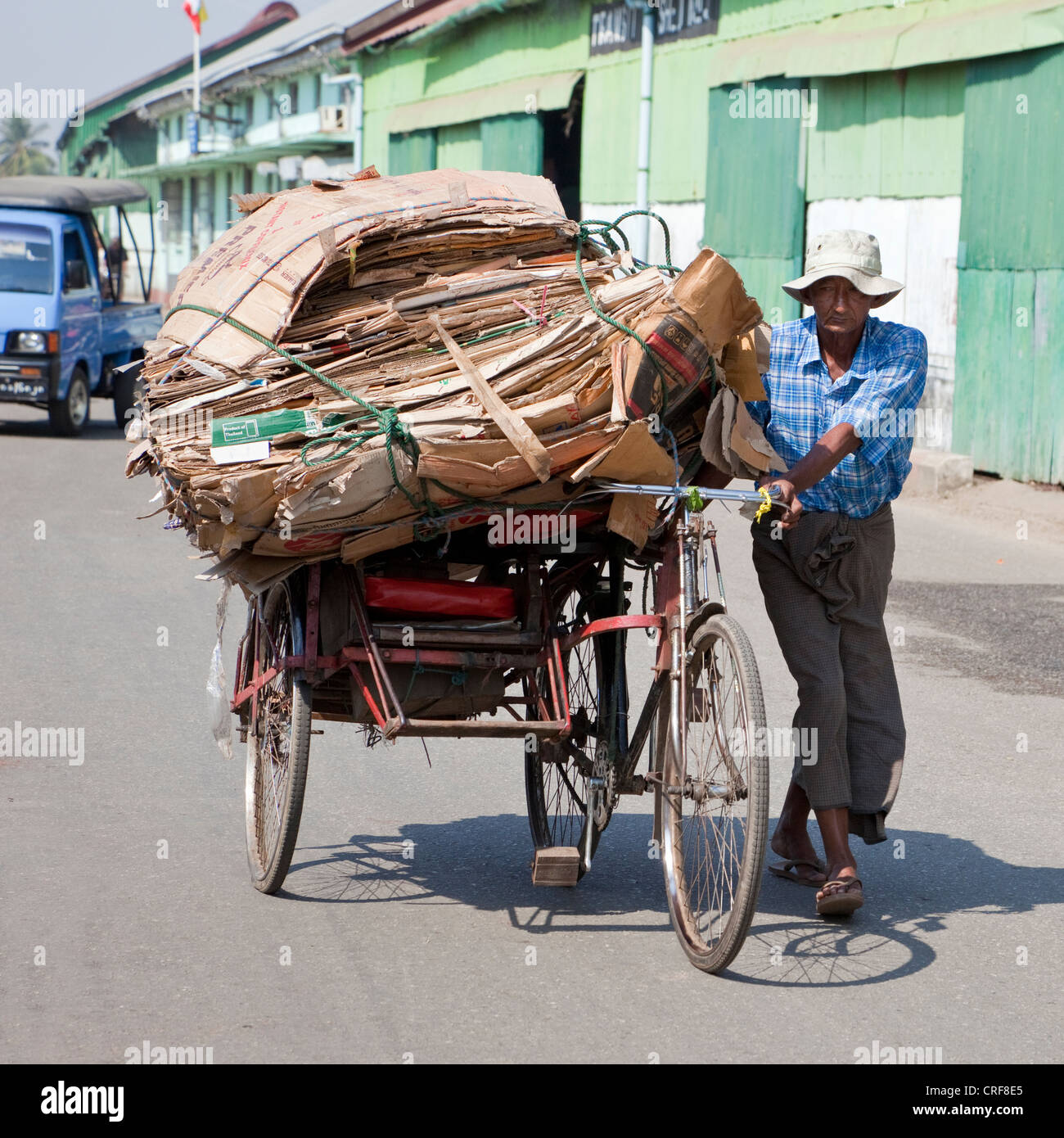 Myanmar Birmania, Yangon. Il riciclaggio. In rickshaw Driver passeggiate un carico di cartoncino ad una stazione di riciclaggio. Foto Stock