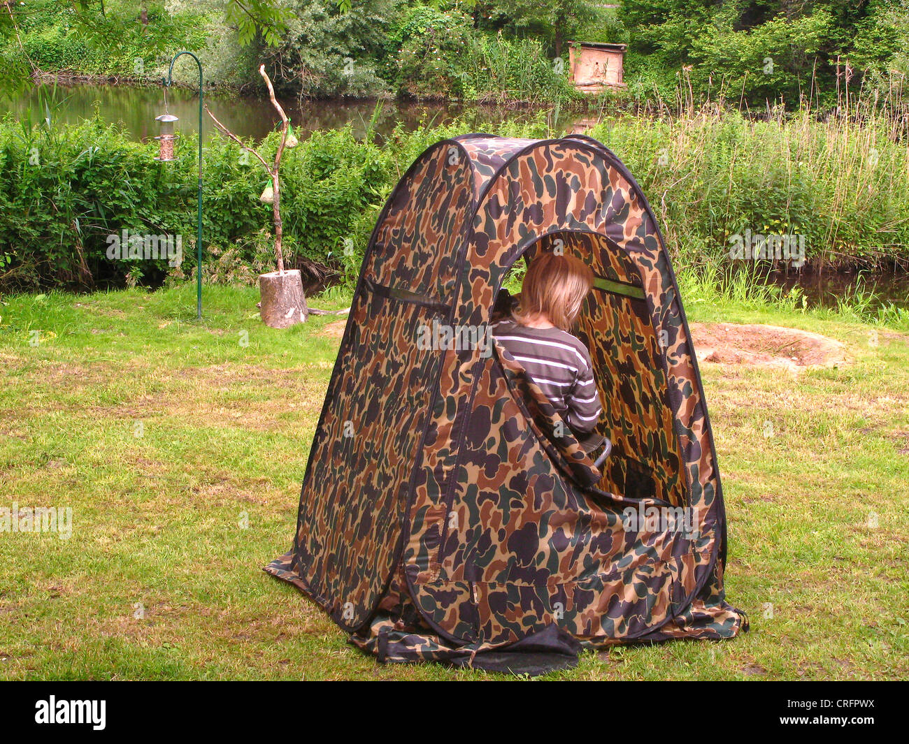 Bambino seduto in camuffamento tenda a guardare gli uccelli, Germania Foto Stock