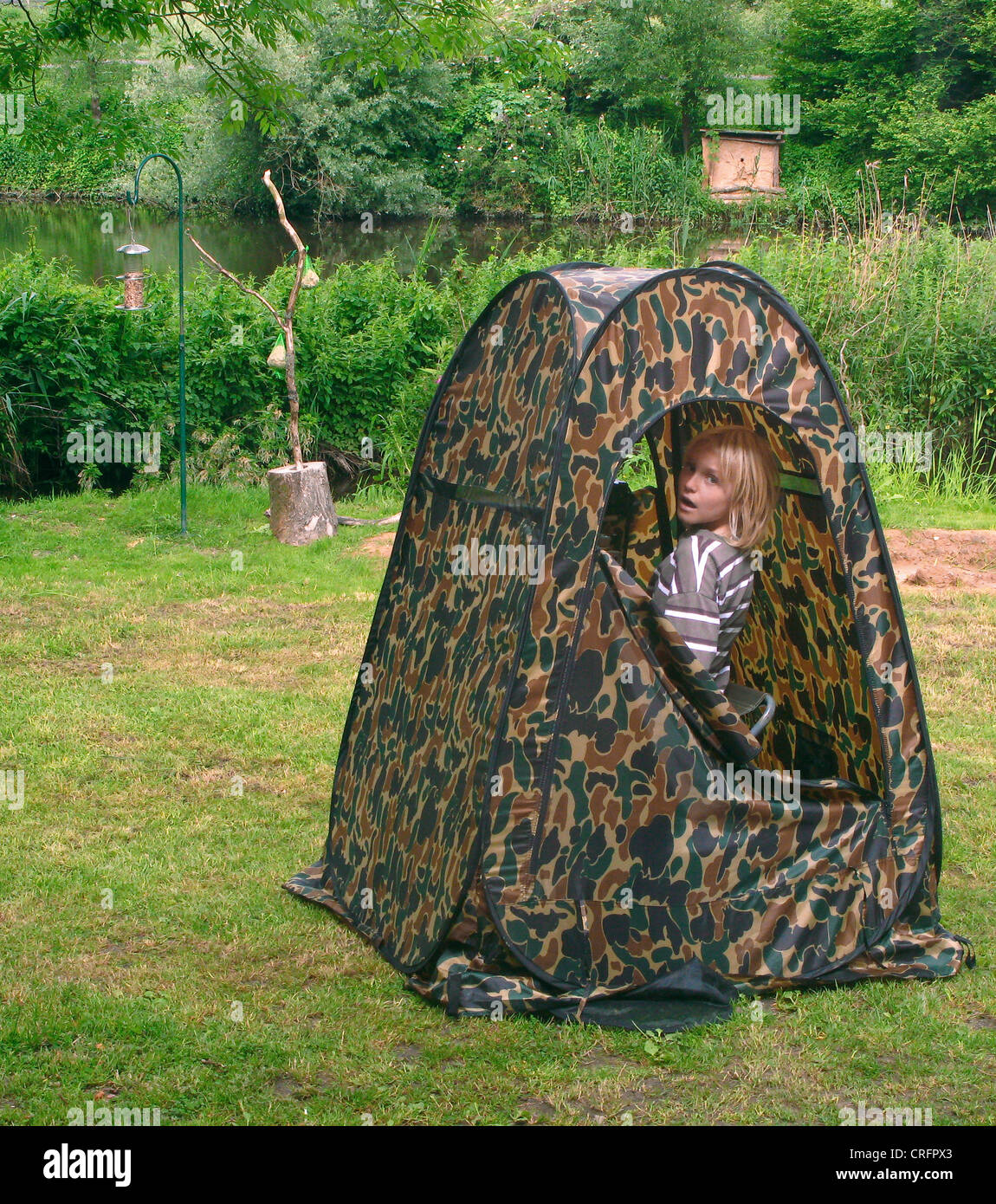 Bambino seduto in camuffamento tenda a guardare gli uccelli, Germania Foto Stock