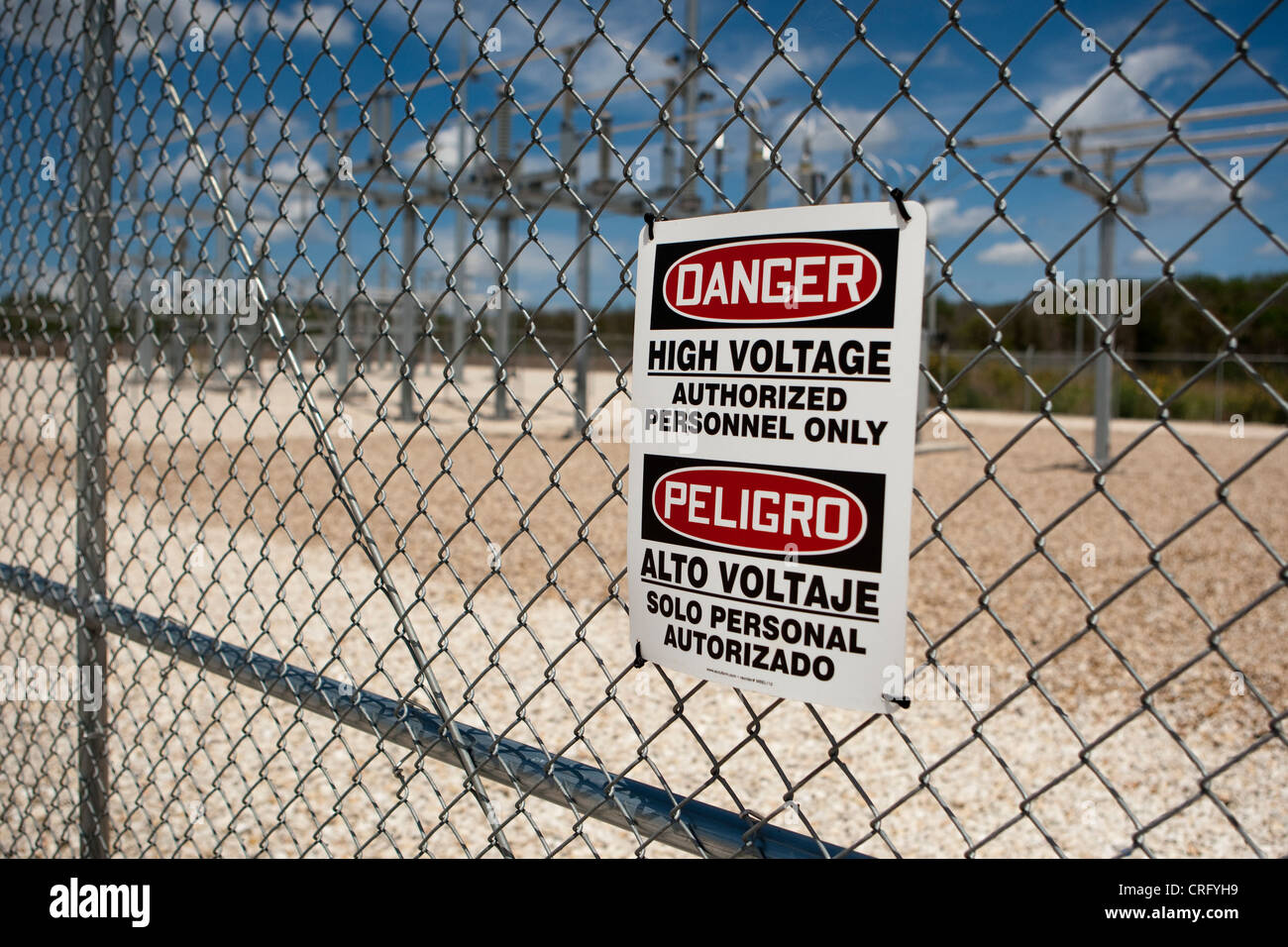 Alta tensione di segno di pericolo sulla catena collegamento recinto a energia solare farm in Texas in inglese e spagnolo Foto Stock