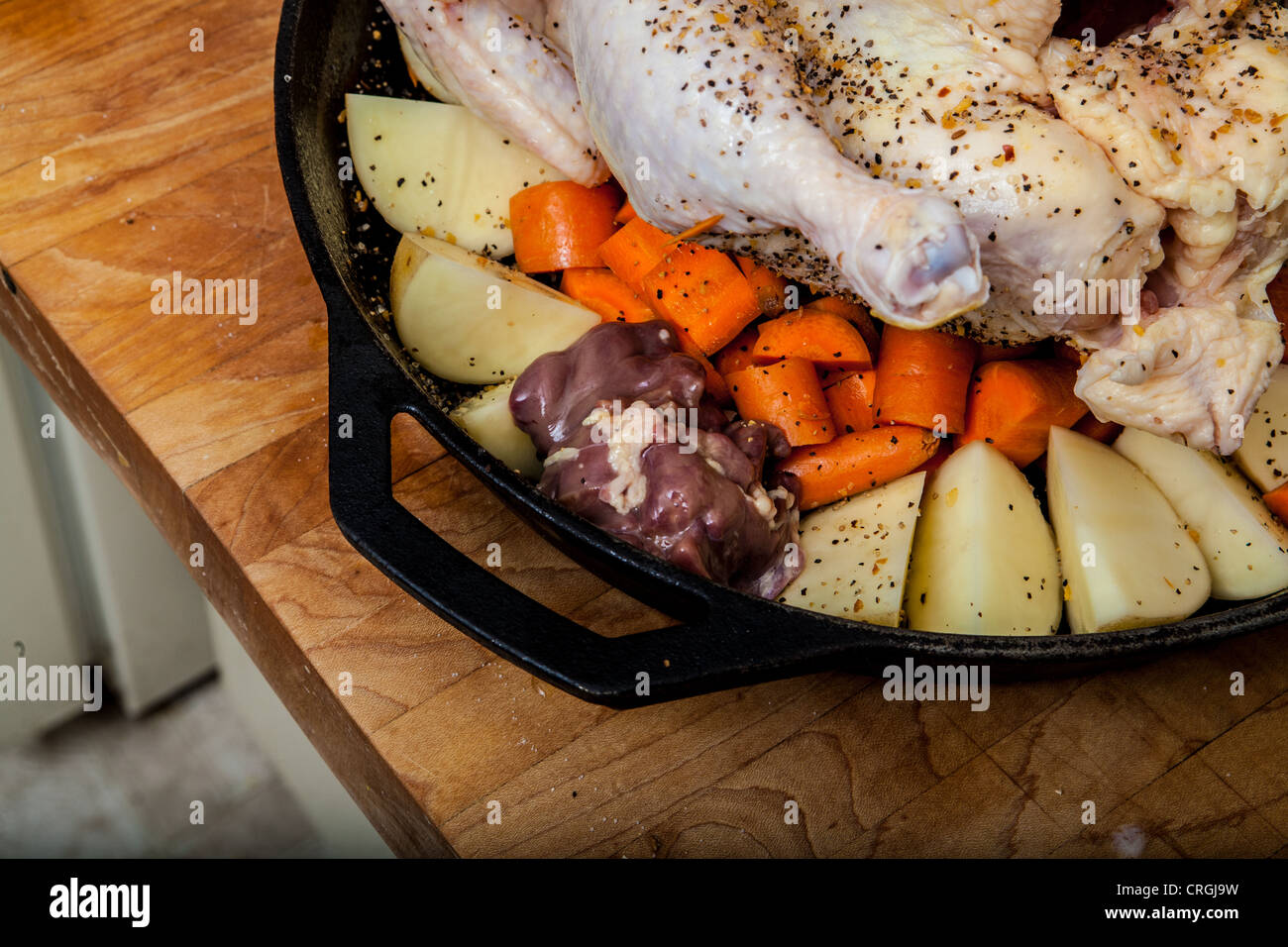 Un pollo crudo preparato per la tostatura con le patate e le carote in una ghisa padella Foto Stock