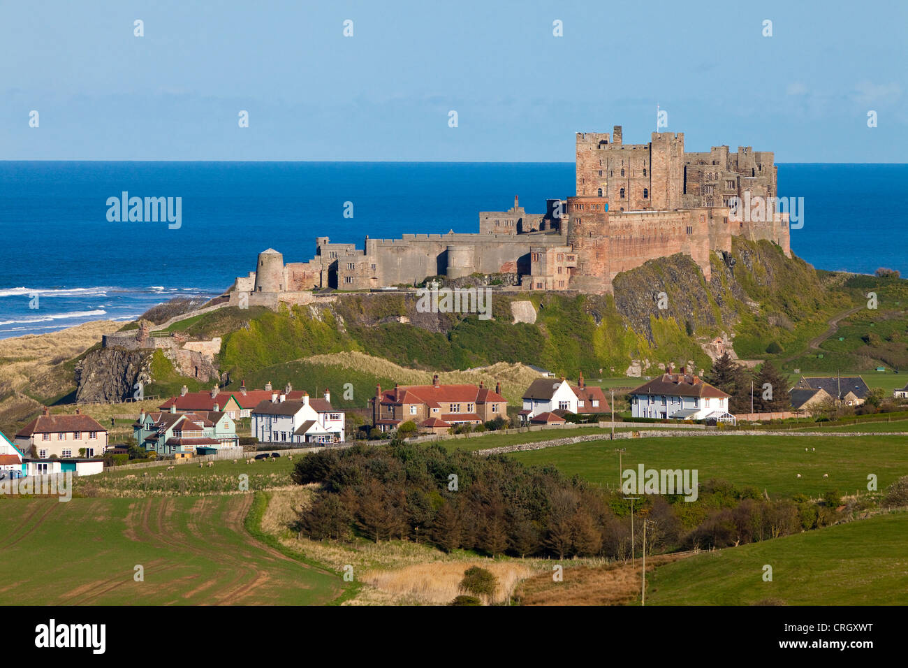 Il castello di Bamburgh, Northumberland, Inghilterra, Regno Unito con le case nel villaggio di Bamburgh in primo piano Foto Stock Il castello di Bamburgh, Northumberland, Inghilterra, Regno Unito con le case nel villaggio di Bamburgh in primo piano Foto Stock