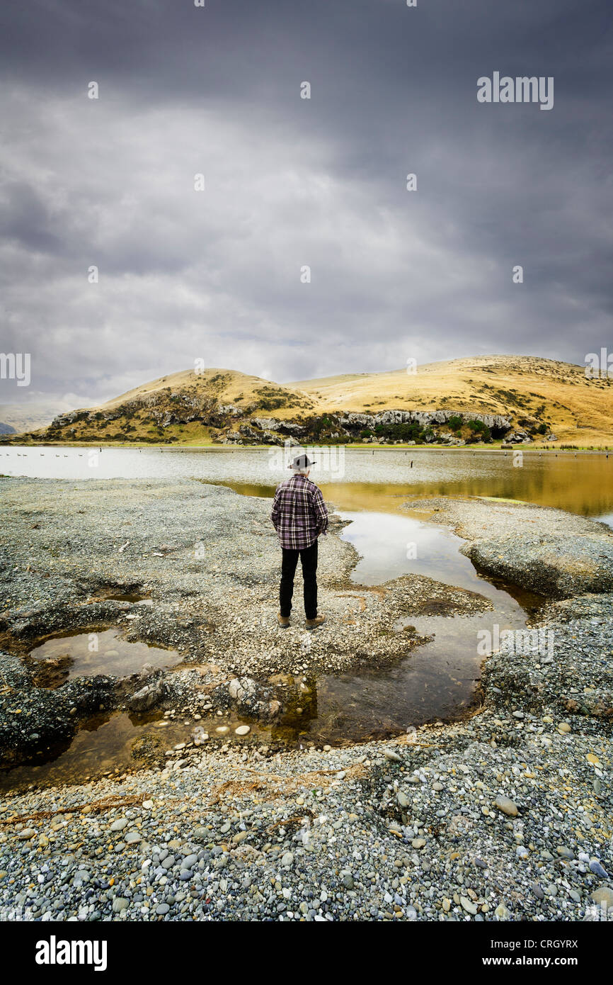 Uomo in piedi in paesaggi selvaggi sotto un cielo meditabondo. Nuova Zelanda, Isola del Sud. Modello di rilascio disponibili. Foto Stock