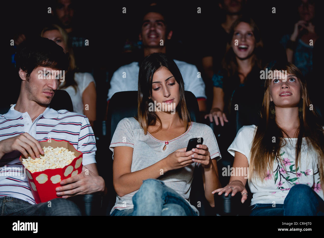 Donna che utilizza il cellulare in movie theater, uomo guardando sopra con l'espressione infastiditi Foto Stock