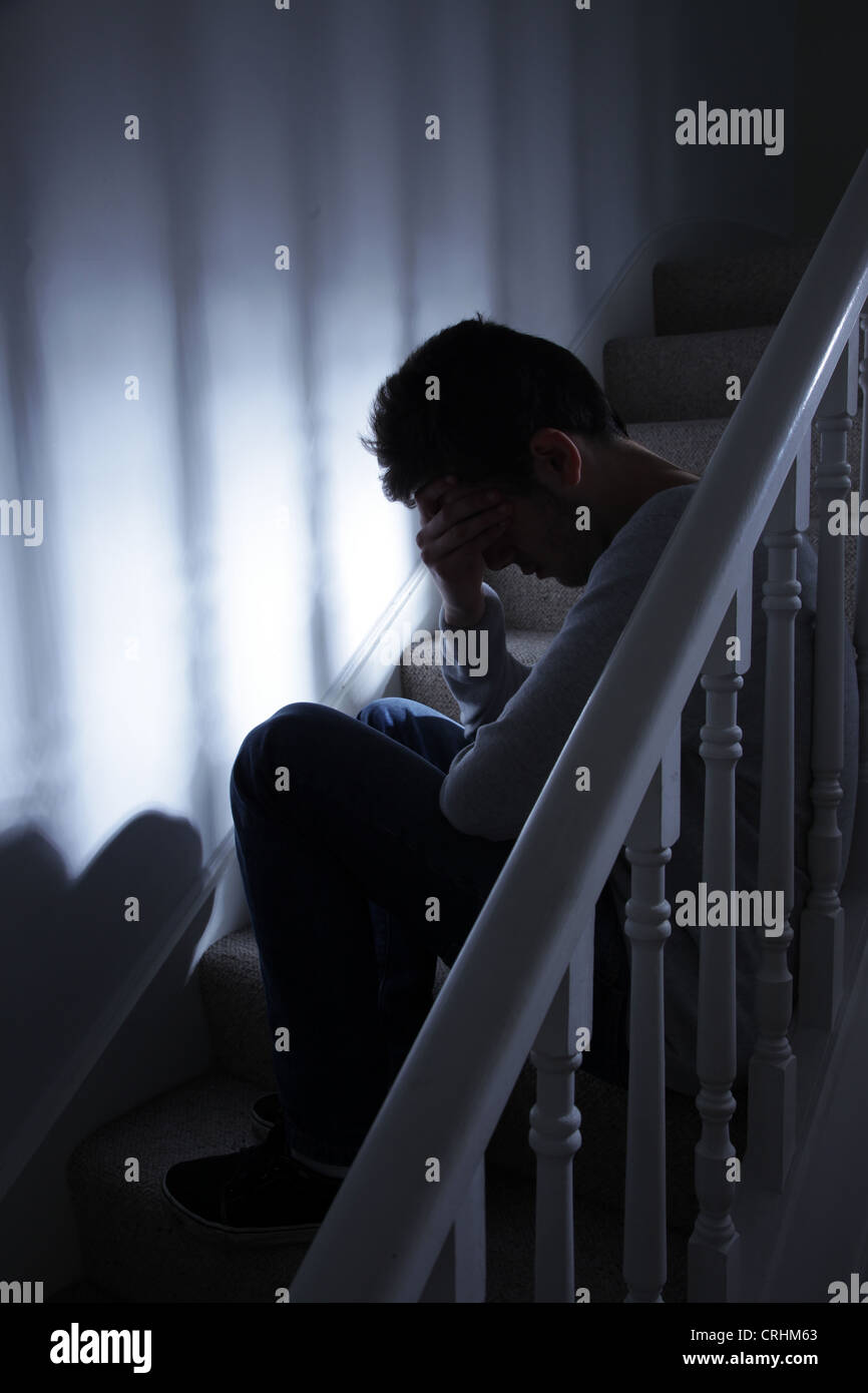 Giovane uomo seduto su per le scale e la sua mano che copre il volto. Foto Stock