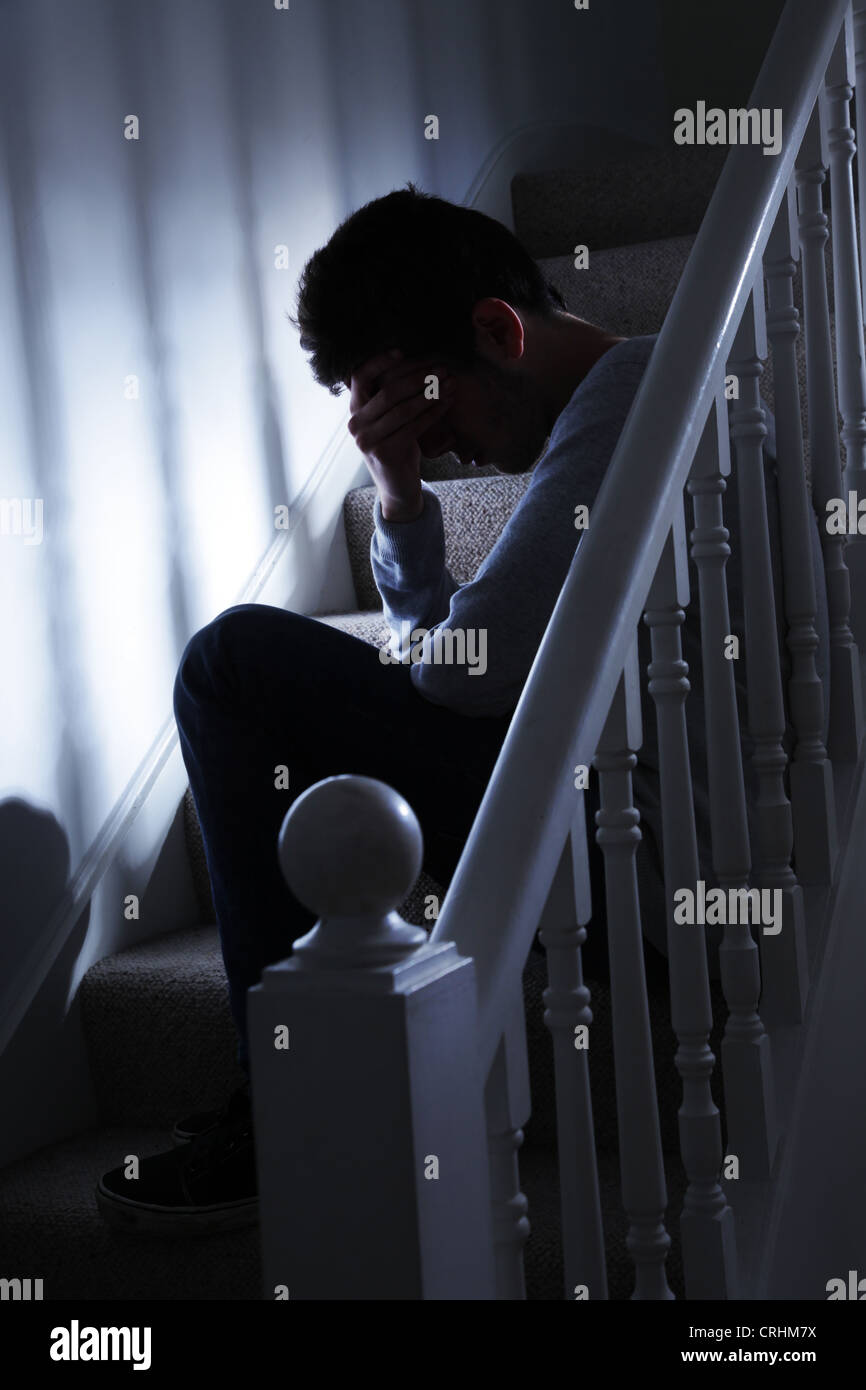 Giovane uomo seduto su per le scale e la sua mano che copre il volto. Foto Stock