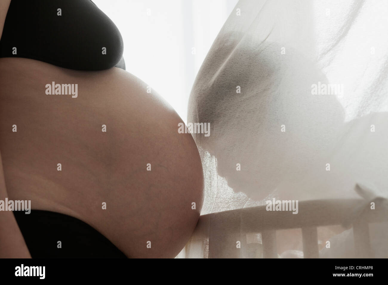 Bambino dietro la cortina, appoggiato la testa sulla madre del ventre in gravidanza, retroilluminato Foto Stock