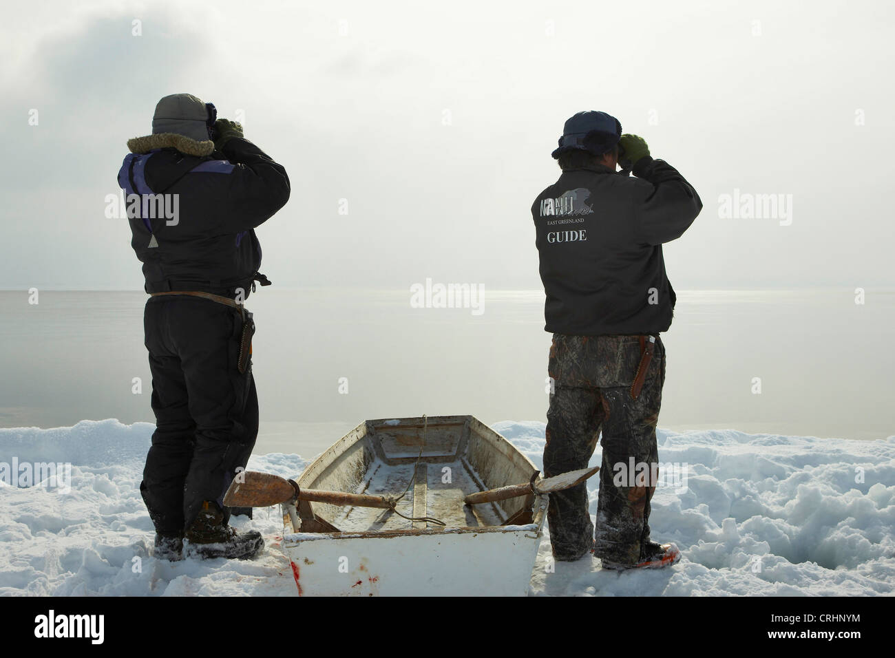 Due saldatori Inuit permanente al bordo di ghiaccio accanto al loro barca a remi e si affacciano sul mare aperto con il binocolo, Groenlandia, Ostgroenland, Tunu, Kalaallit Nunaat, Scoresbysund, Kangertittivag, Kap Tobin, Ittoqqortoormiit Foto Stock