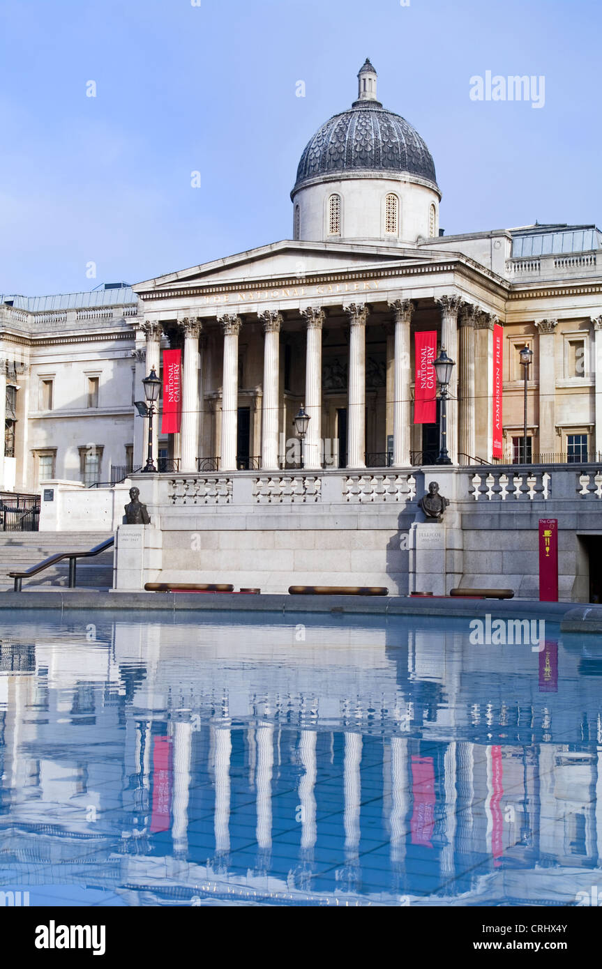 Vista frontale della National Gallery di Londra, riflessa nell'acqua ancora di una piscina con fontana, Trafalgar Square, la mattina presto. Foto Stock