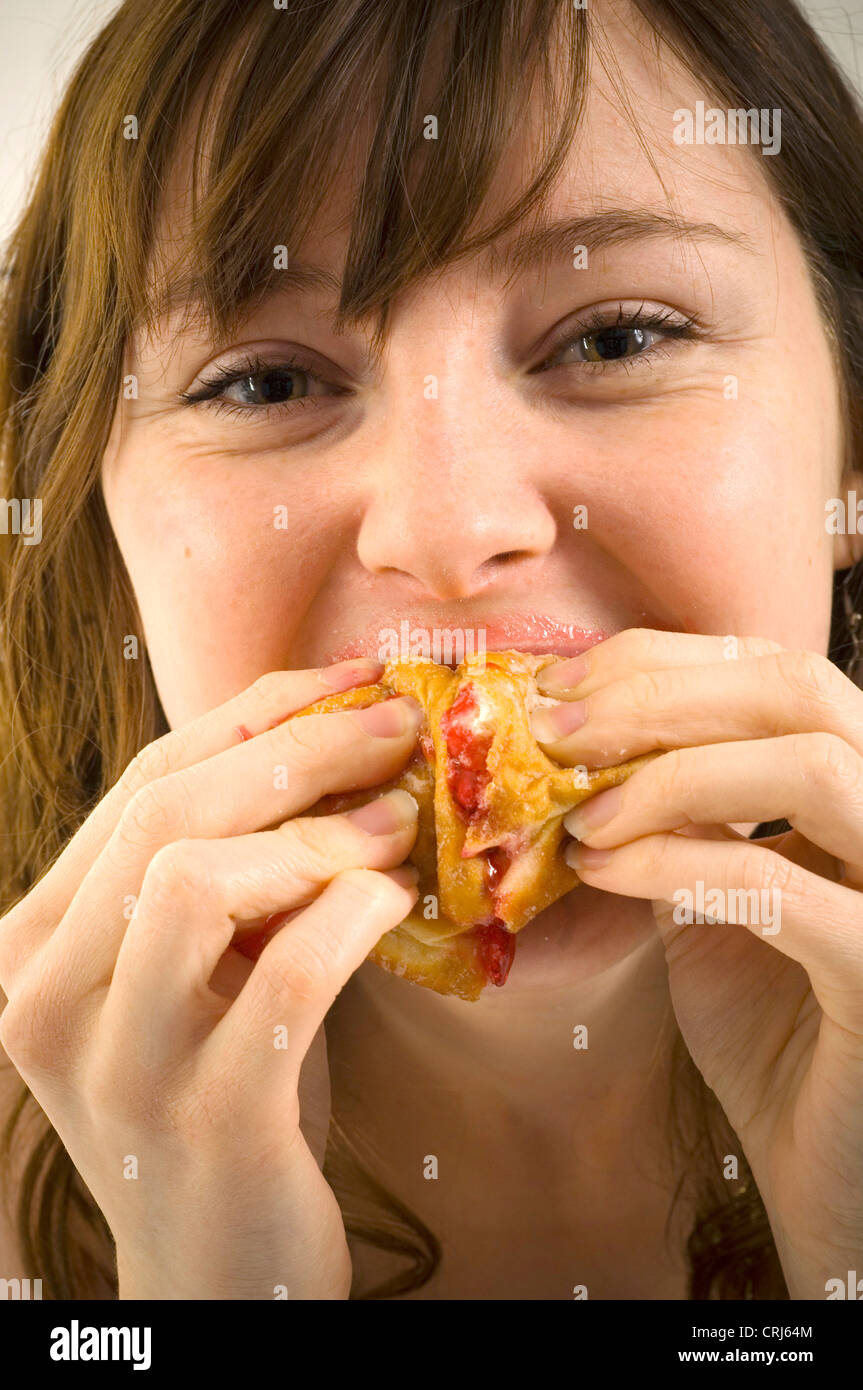 Un giovane femmina imbottisce la sua bocca piena di ciambelle con marmellata. Jam Donut hanno criticato dal cibo spazzatura gli attivisti in guerra globale sull'obesità come insalubre con scarso valore nutrizionale. Il termine "junk food" è stato coniato da Michael Jacobson, Direttore del Centro per la scienza nel pubblico interesse, per descrivere il cibo che conteneva contengono livelli elevati di grassi saturi, Foto Stock