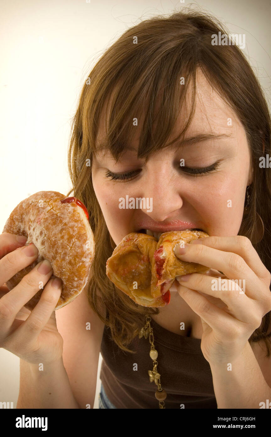 Un giovane femmina imbottisce la sua bocca piena di ciambelle con marmellata. Jam Donut hanno criticato dal cibo spazzatura gli attivisti in guerra globale sull'obesità come insalubre con scarso valore nutrizionale. Il termine "junk food" è stato coniato da Michael Jacobson, Direttore del Centro per la scienza nel pubblico interesse, per descrivere il cibo che conteneva contengono livelli elevati di grassi saturi, Foto Stock