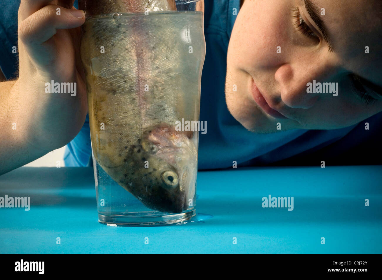 Giovane uomo orologi un pesce in un bicchiere d'acqua. L'acqua, l'elisir di lunga vita e un pesce, la fonte primaria di omega-3, considerata come un importante beneficio per la salute. Foto Stock